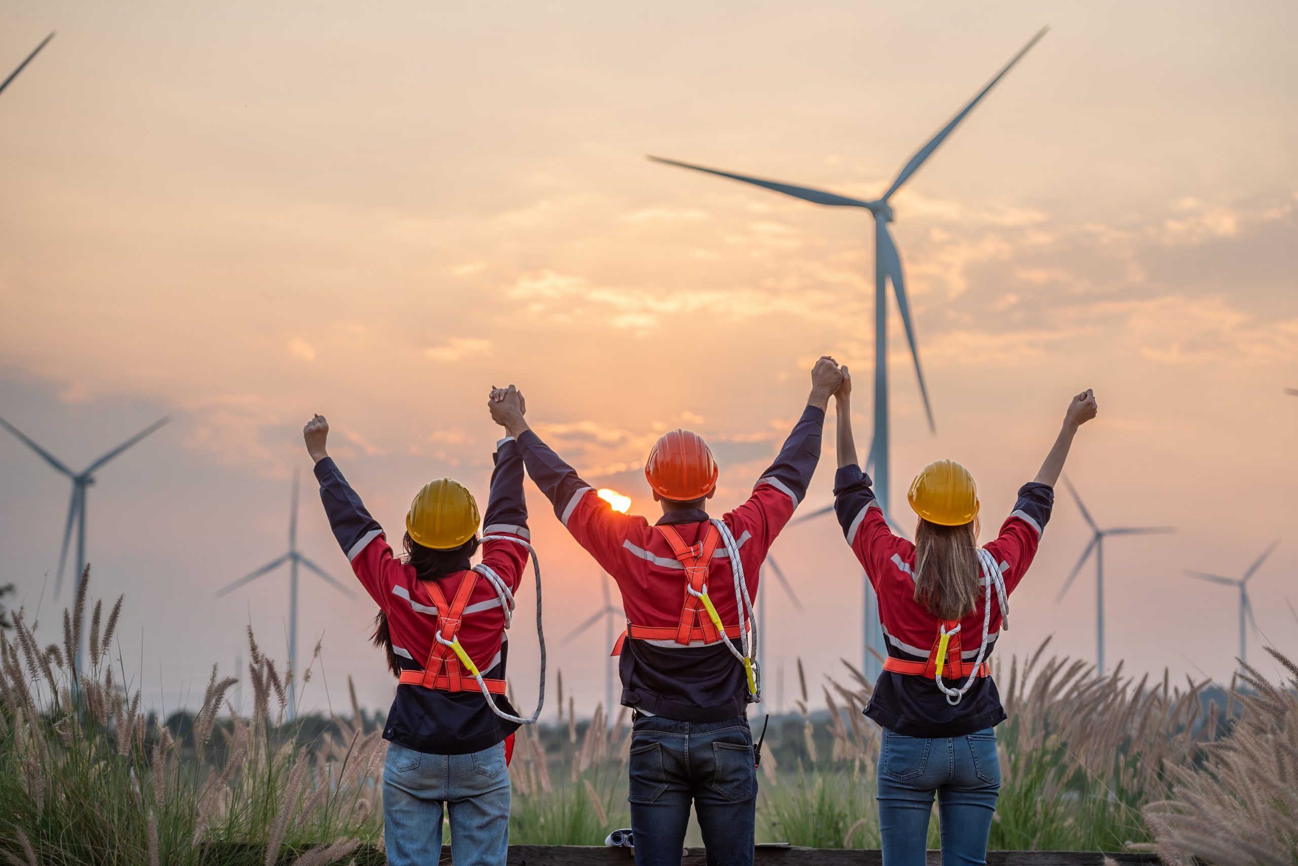 Three people are standing in a field with wind turbines in the background